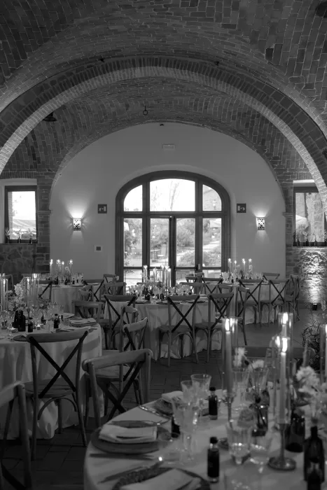 Reception room at Borgo Sant Ambrogio with candlelit tables and a large arched window overlooking the Tuscan landscape.