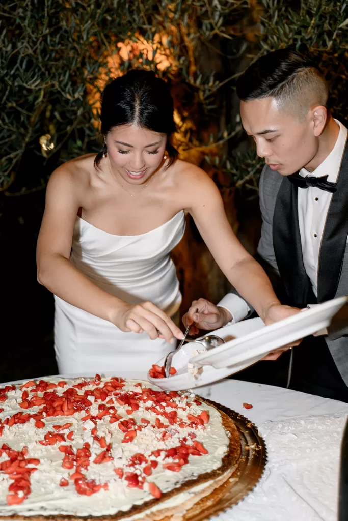 Bride adds strawberries to a large cream-filled dessert during an outdoor celebration at Borgo Sant Ambrogio.