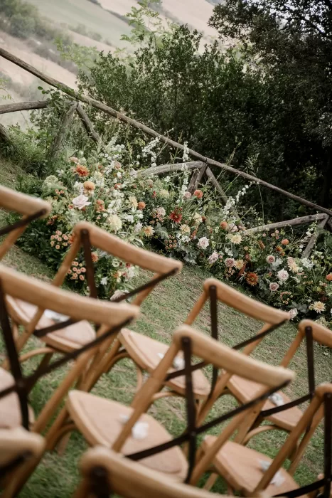 Angled view of wooden chairs and vibrant floral aisle bordering a rustic countryside ceremony at Borgo Sant'Ambrogio.