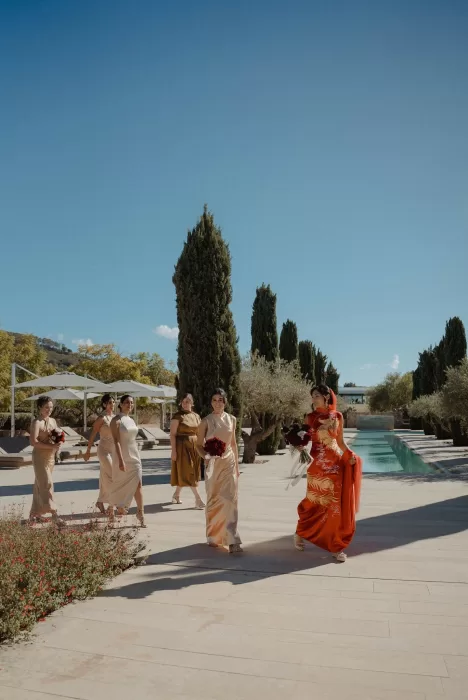 Bride and bridesmaids walking by the pool at Ca Na Xica in red and gold ceremony attire