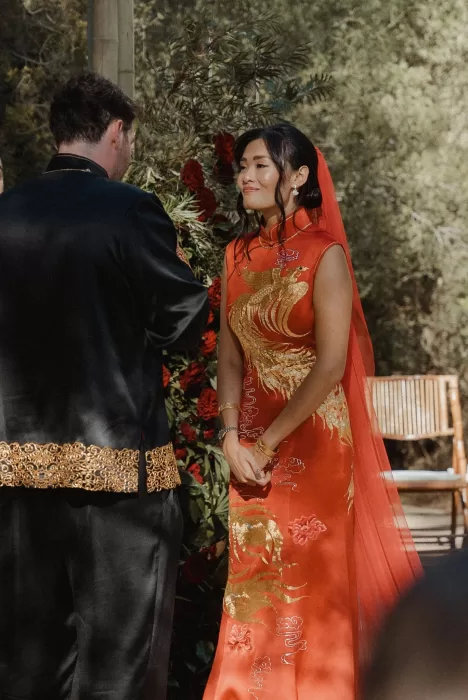Bride gazing at groom during vows, framed by red florals and soft natural light at Ca Na Xica