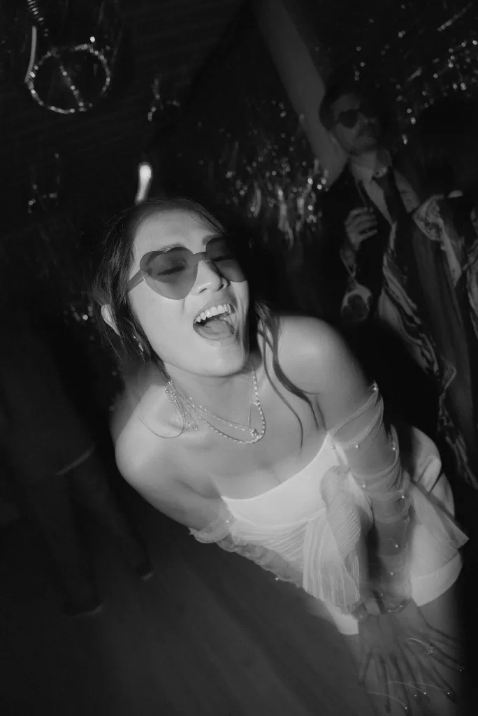 Playful moment of the bride in heart-shaped sunglasses laughing on the dancefloor at Ca Na Xica.