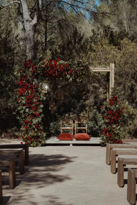 Outdoor wedding altar with bamboo chairs and lush red floral arch at Ca Na Xica woodland ceremony space.