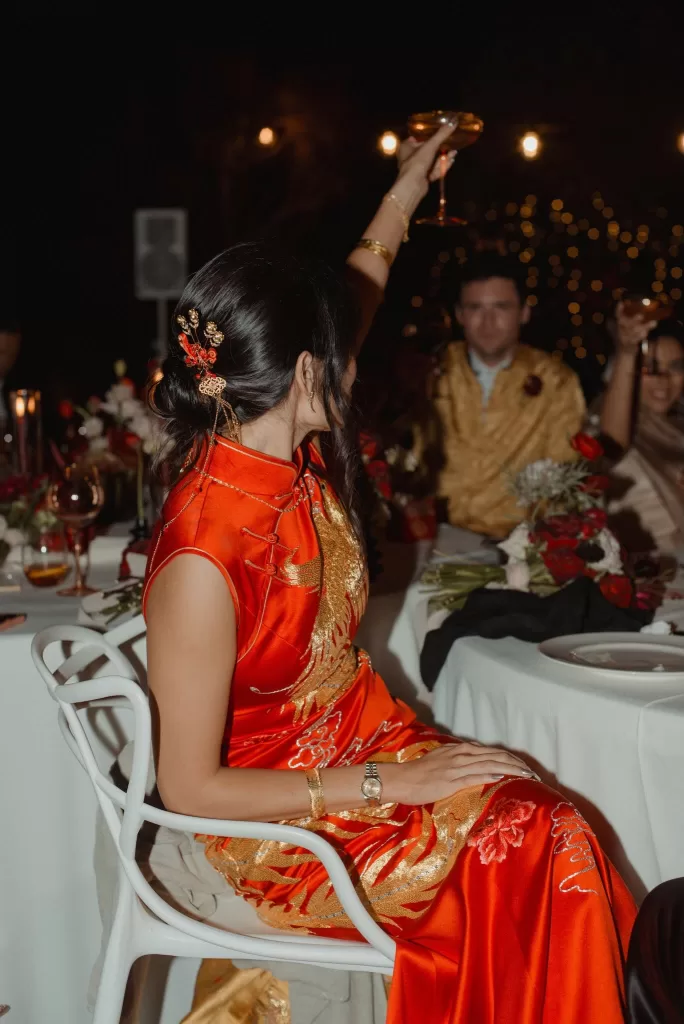 Bride in red and gold cheongsam raising a toast during wedding dinner at Ca Na Xica