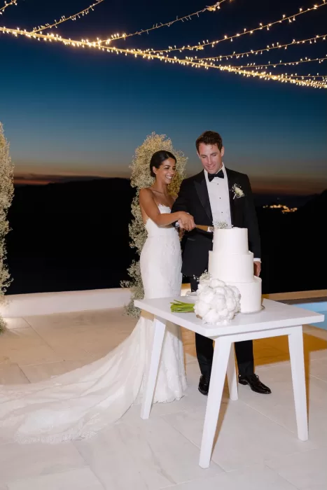 Bride and groom cut their wedding cake against the glowing Santorini skyline