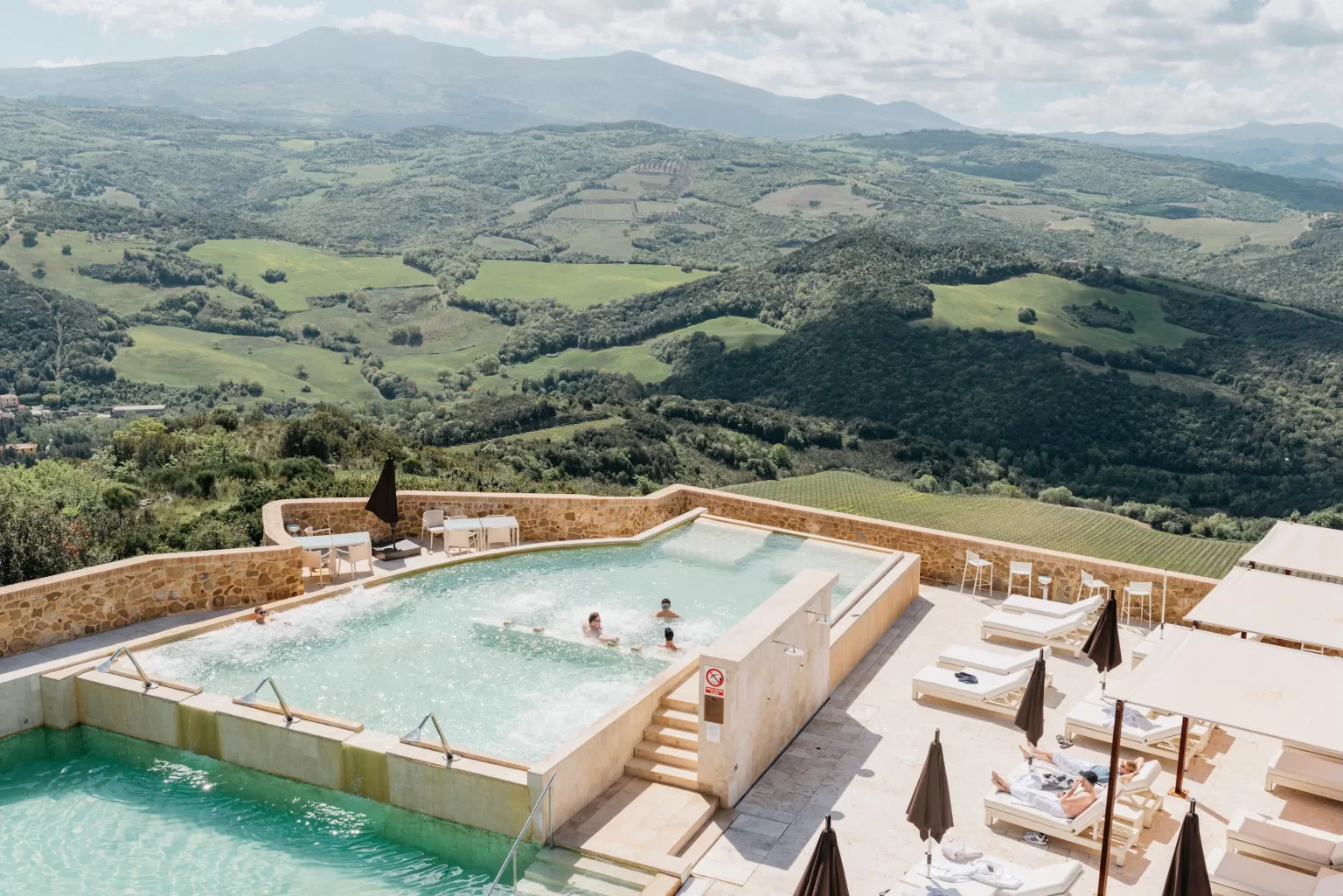 Guests relaxing in the thermal pools at Castello di Velona with rolling Tuscan hills in the background.