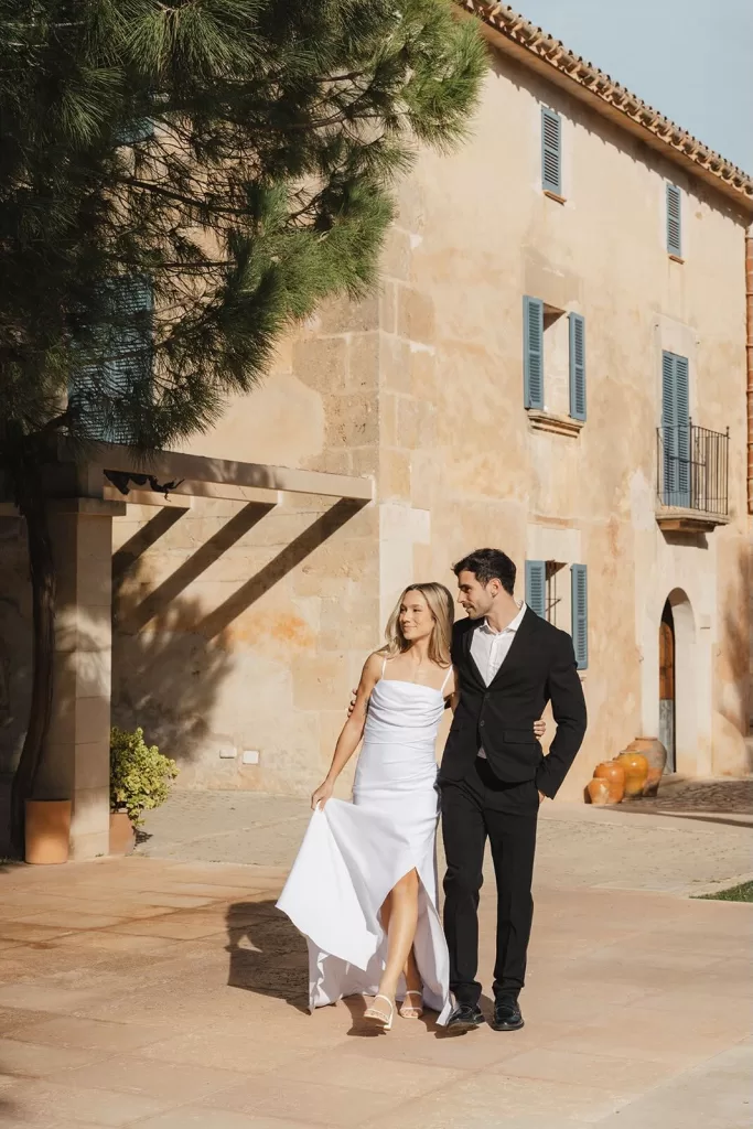 Bride and groom walking arm in arm by the rustic façade of Finca Son Sampol