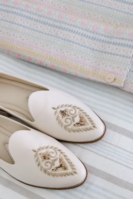 Elegant cream loafers with gold embroidery next to a pastel sherwani at Masia Casa del Mar.