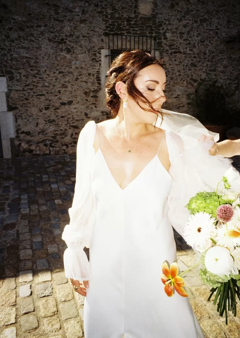 Bride in modern gown holding bouquet, captured in film-style light outside Mas Torroella