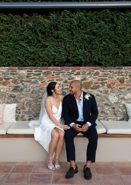 Bride and groom sharing a quiet moment on a stone bench at Mas Torroella, with lush greenery behind them