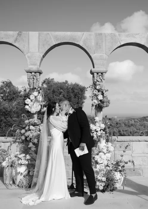 The newlyweds share their first kiss as confetti floats around the floral altar at Mas Torroella.