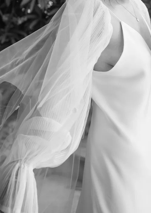 Close-up in black and white capturing the airy tulle sleeves and smooth satin texture of the bride’s gown.