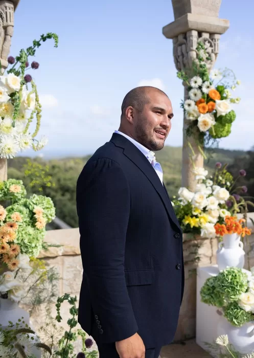 The groom waits at the ceremony altar at Mas Torroella, surrounded by wild, vibrant flowers and sweeping views.