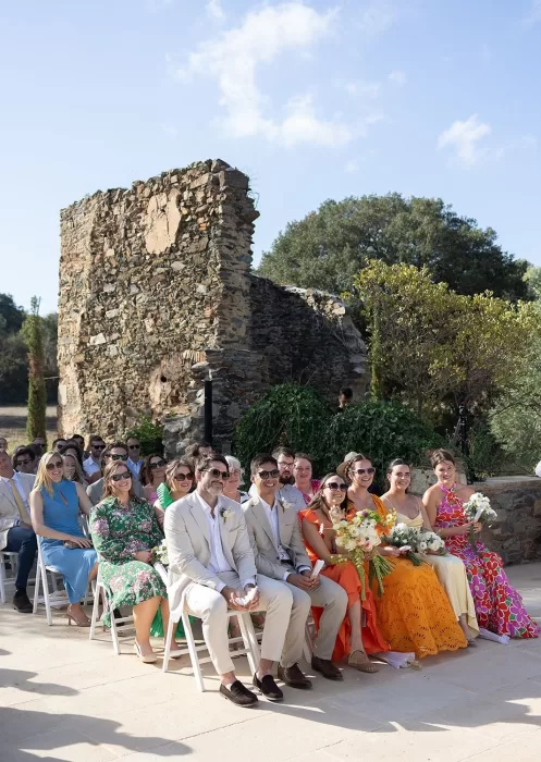 Guests in colourful outfits enjoy the sunshine during the outdoor ceremony at Mas Torroella.