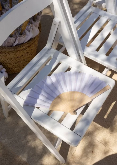 Wooden hand fan placed on a white ceremony chair under dappled sunlight at Mas Torroella.