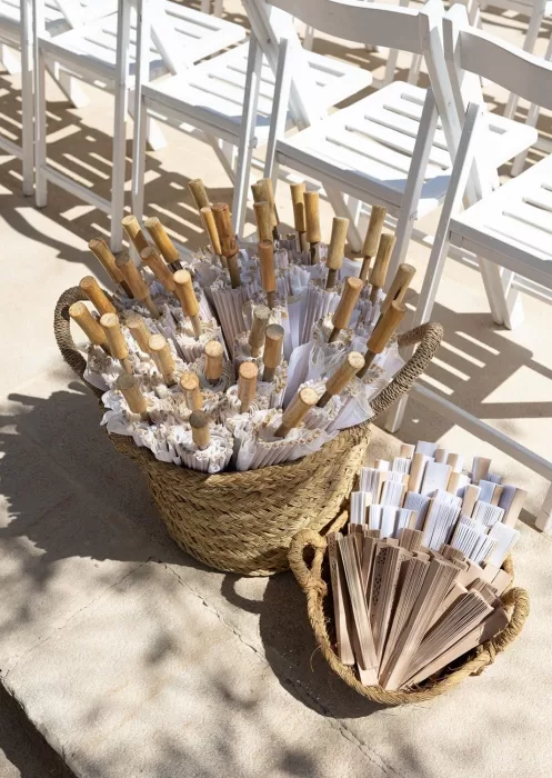 White parasols and wooden fans ready for guests at a summer wedding at Mas Torroella.