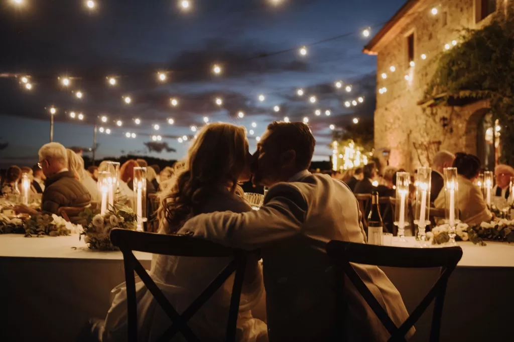 Bride and groom share a kiss at their candlelit reception dinner under string lights at Podere Calvaiola.