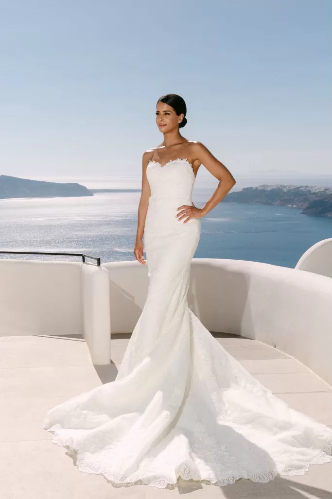 Full-length bridal portrait with Santorini’s blue horizon and Rocabella architecture in frame