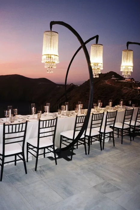 Elegant long dinner table under modern chandeliers with a sunset view of the cliffs at Rocabella Santorini.