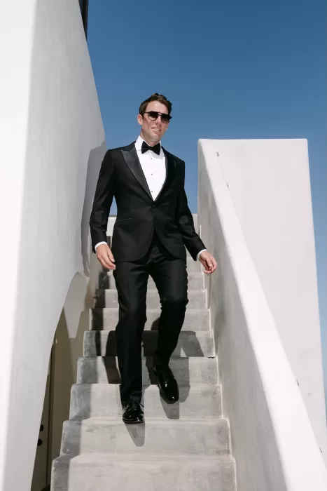 Stylish groom poses on whitewashed stairs at Rocabella Santorini