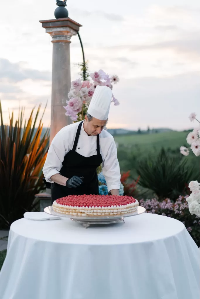 Chef preparing a large raspberry tart on a white table outdoors at Tenuta Corbinaia as the sun begins to set.