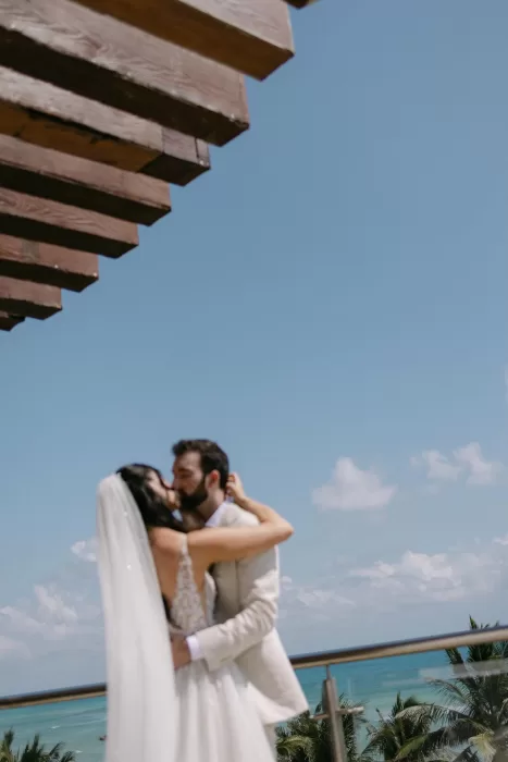 Bride and groom share a kiss overlooking the sea from a balcony at Villa La Joya.