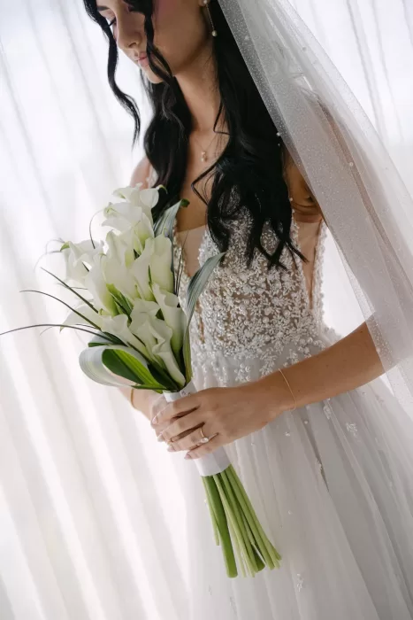 Bride holding elegant white calla lily bouquet at Villa La Joya, her embellished gown softly lit by natural light.