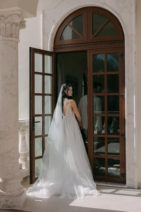 Bride glancing back as she steps through a grand wooden doorway at Villa La Joya.
