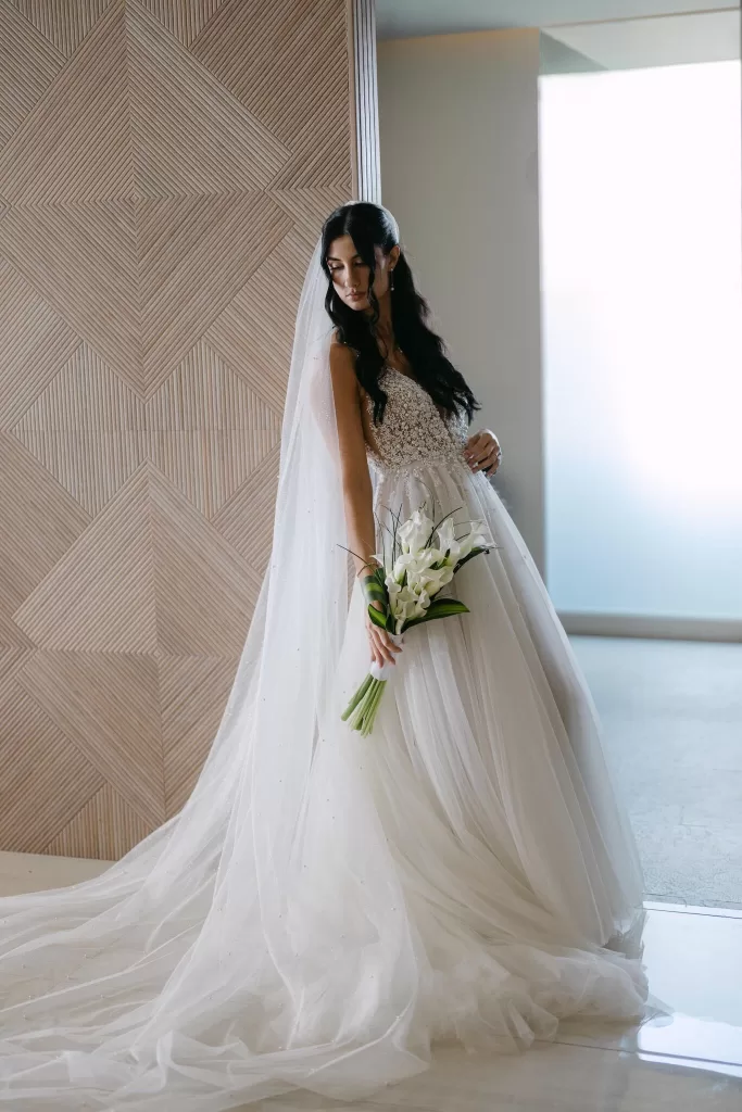 Bride in flowing gown with long veil and calla lilies, standing in modern interior at Villa La Joya.