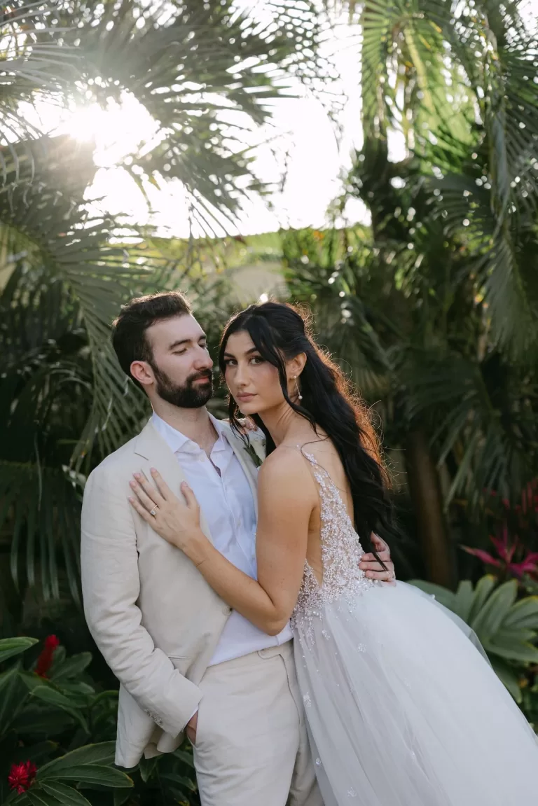 Bride and groom pose among tropical greenery in golden hour light at Villa La Joya.