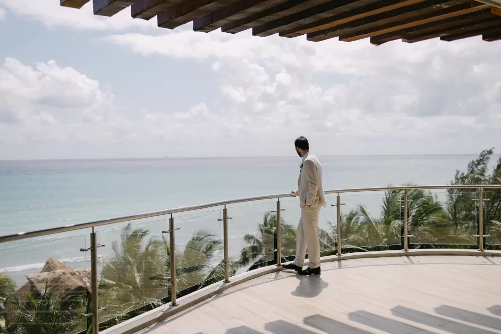 Groom in light suit gazing over the sea from modern balcony at Villa La Joya.