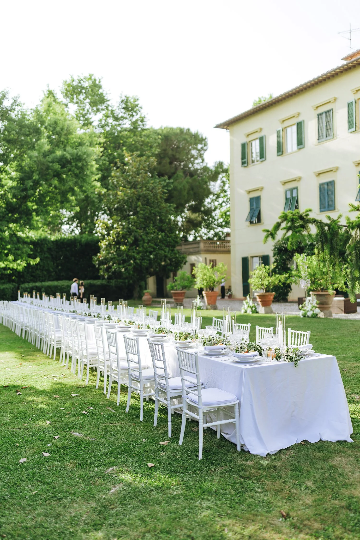 Elegant white tables and chairs set for an outdoor wedding reception on the lawn of Villa Ravano.