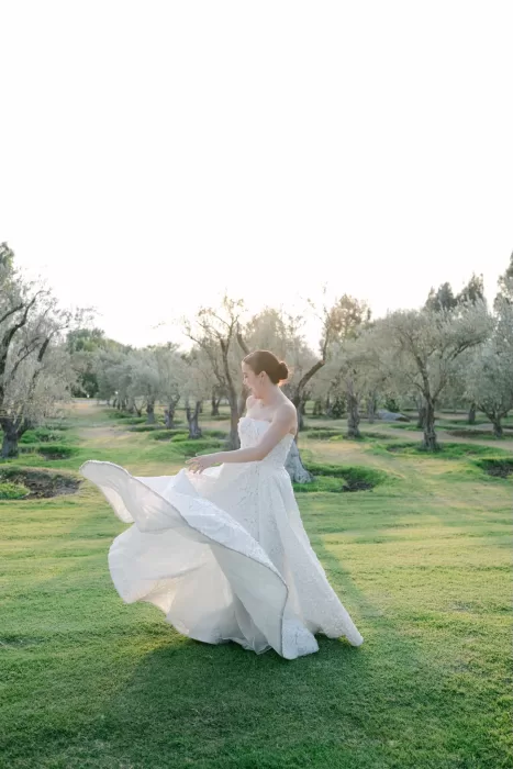 Bride twirling joyfully in open green field surrounded by olive trees at Luna Escondida.