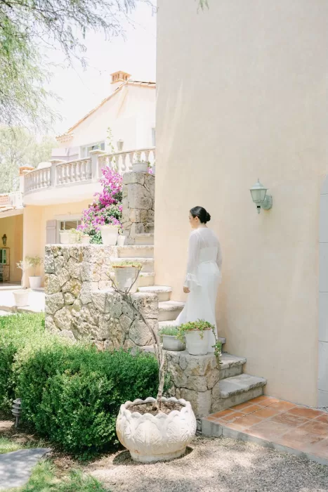 Bride in white robe ascending rustic stone garden stairs surrounded by potted plants at Luna Escondida