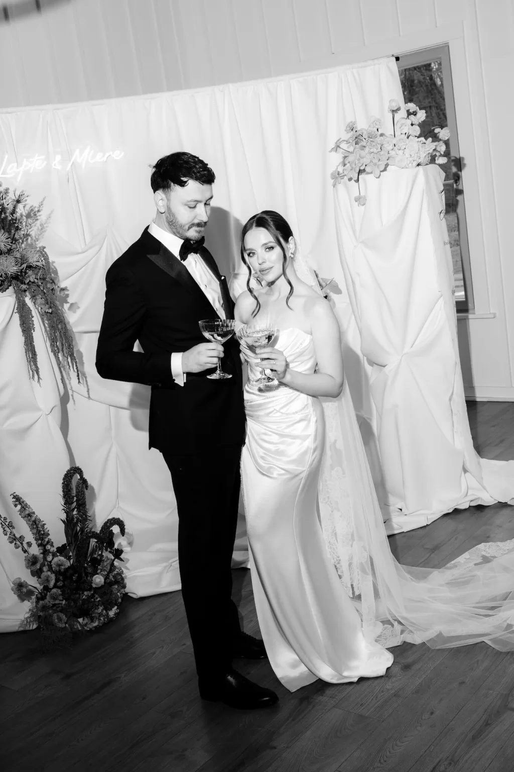 Black and white image of bride and groom sharing a toast at stylish wedding altar.