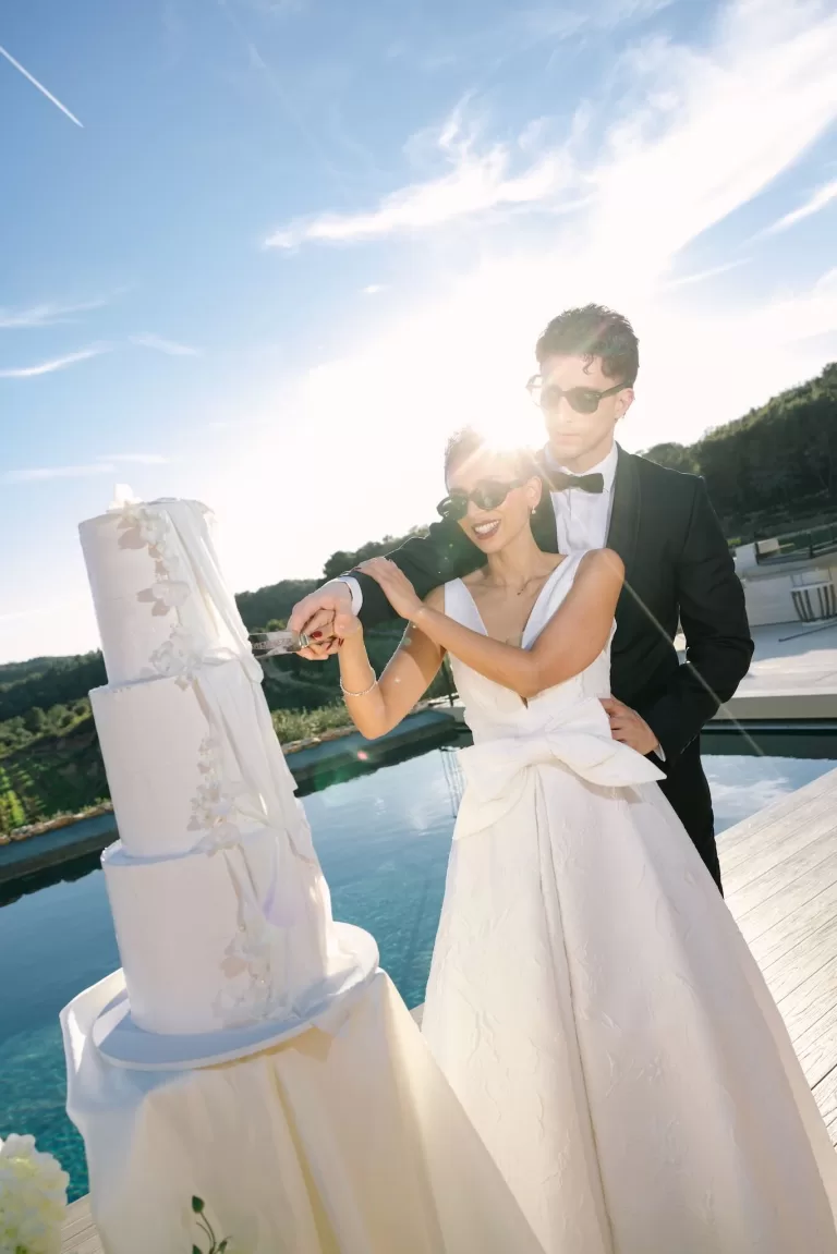 Bride and groom cut cake beside the pool at Masia Cabellut as the sun sets behind them.
