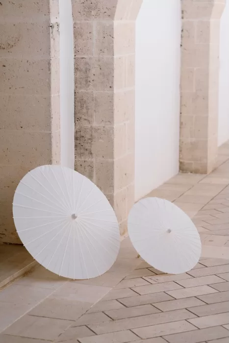 Two white paper parasols leaning elegantly against a stone archway at Masseria San Giovanni.