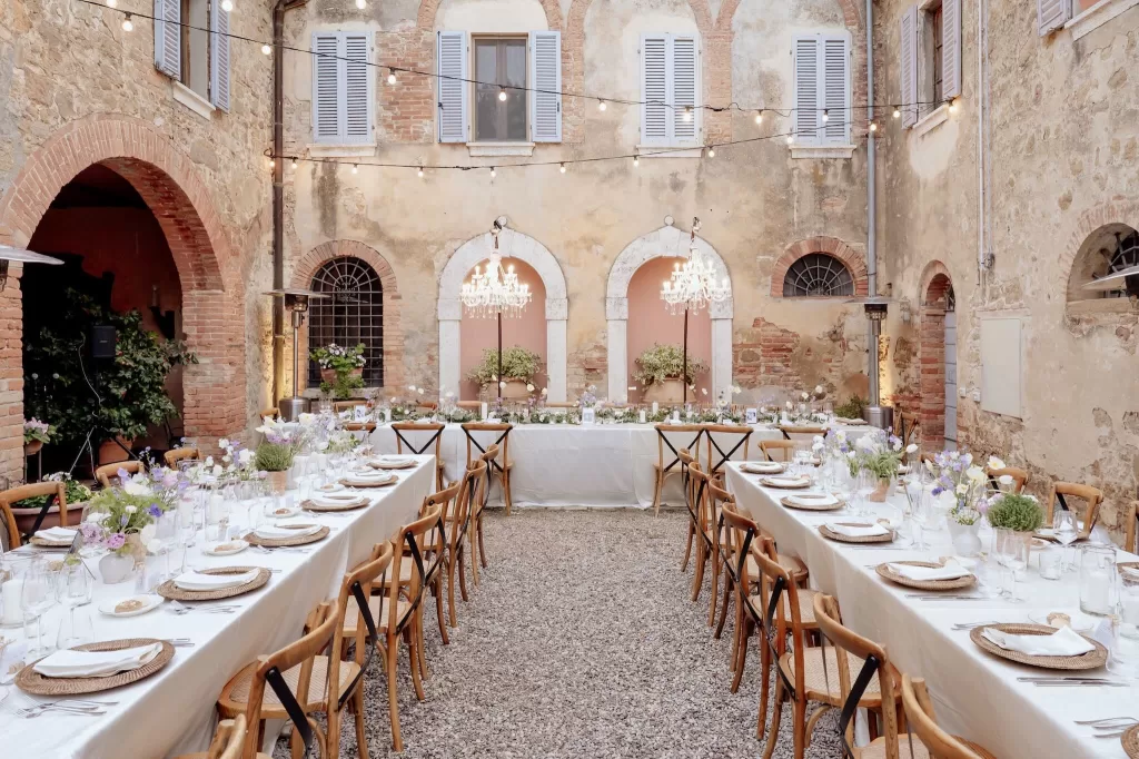 Romantic courtyard setup with chandeliers, rustic walls, and flower-filled tables at Borgo Sant'Ambrogio.