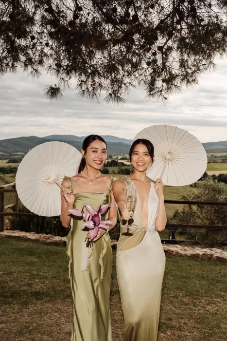 Wedding guests in satin dresses holding white parasols with scenic views at Conti di San Bonifacio.