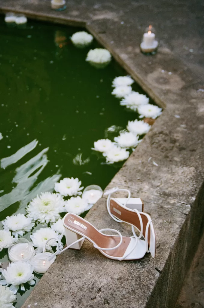 Bridal heels resting beside a candlelit pond with floating white flowers at Finca Es Convent.