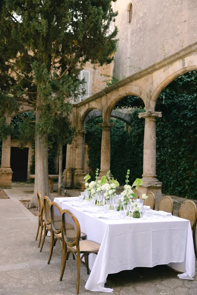 Long wedding table styled with florals beneath the historic arches of Finca Es Convent’s cloister.