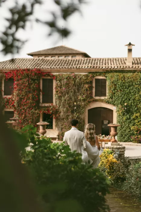 Couple walking hand in hand toward ivy-covered villa at Finca Son Collell