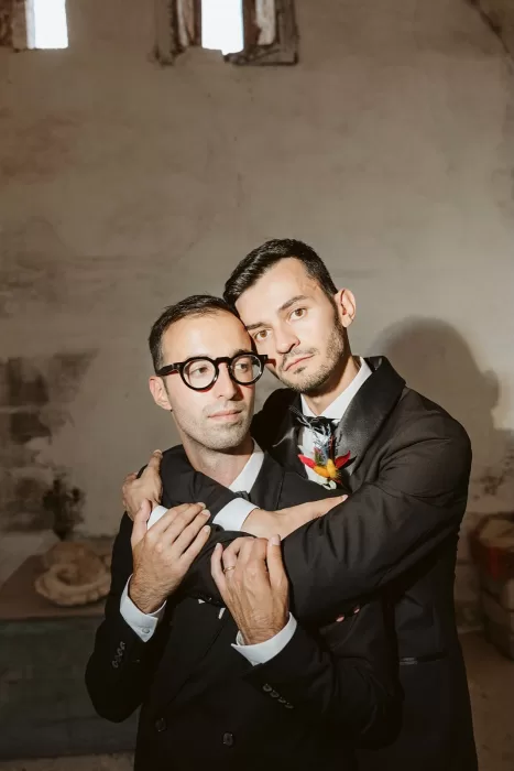 Grooms sharing an emotional embrace in a softly lit room at Masseria Spina.