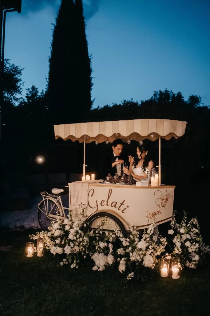 Bride and groom enjoy gelato under candlelight at a vintage cart during Villa Olimpia wedding