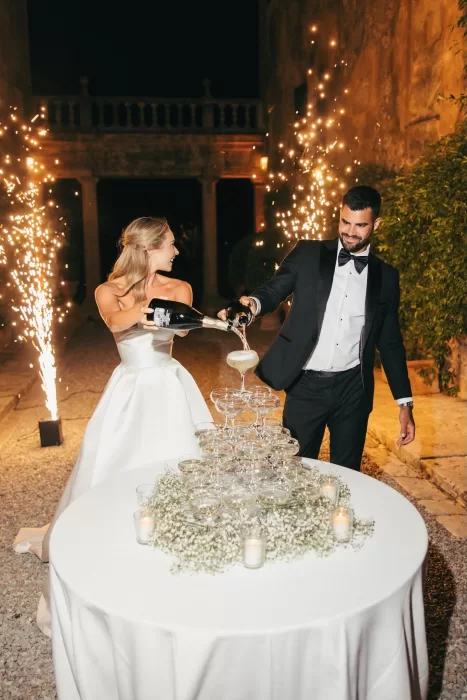 The couple pour champagne in front of dramatic fireworks at night at Borgo Stomenanno.