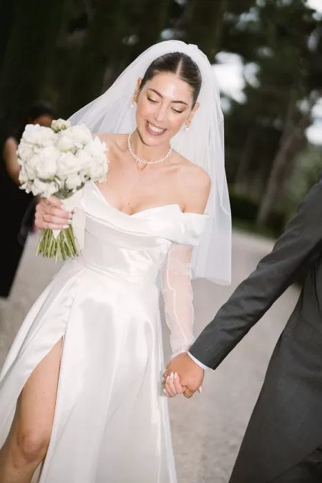 The bride smiles joyfully while holding her bouquet, walking hand in hand with her groom at Cigarral de la Mercedes.