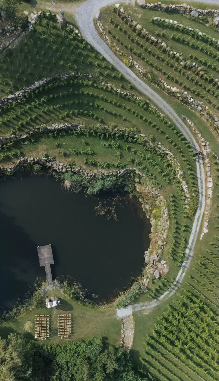 Aerial view of terraced vineyards and lakeside ceremony setup at Château Ste. Agnès, surrounded by lush greenery and curved stone paths.