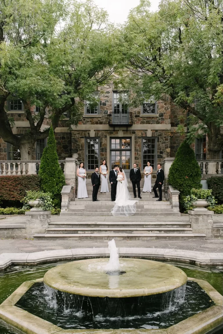 Bride and groom with their wedding party gathered by the fountain and stone steps of Graydon Hall.