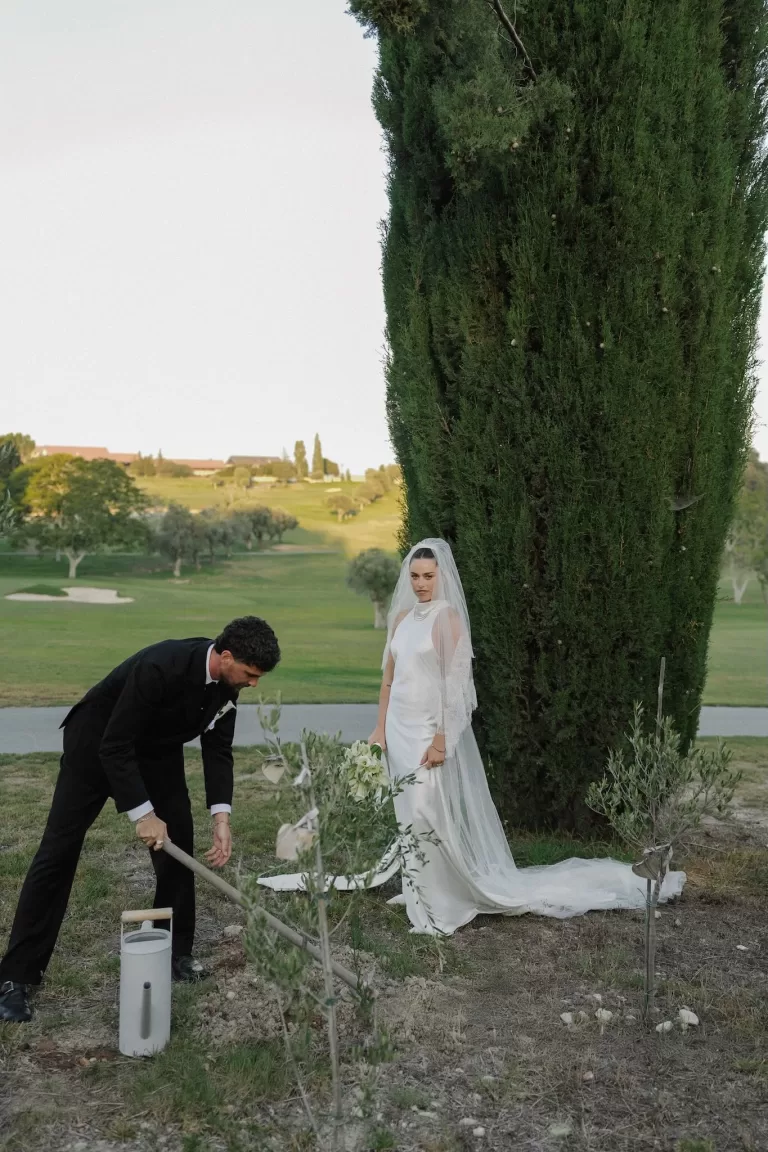 Groom planting a tree while the bride watches during an outdoor ceremony at Minthis Resort.