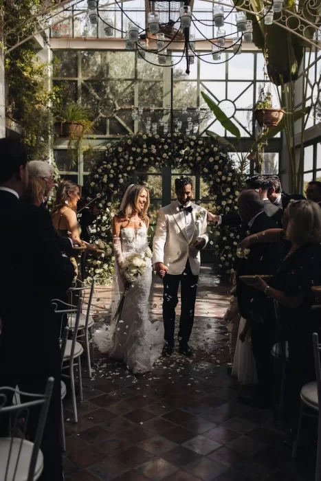 Bride and groom walking back down the aisle under a flower petal toss at Beldi Country Club greenhouse.